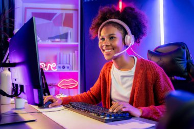 Neon renkli aydınlatma odasında kulaklık takan Afrika kökenli Amerikalı kız flamalı Esport yetenekli takımıyla online dövüş yapıyor. Rakiplerini kazanmak için strateji planlayan diğer oyuncularla konuşmak. Tatlandırıcı.