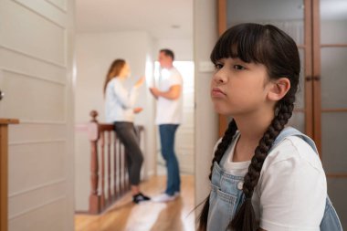 Stresli ve mutsuz genç kız arka planda ebeveynleri tartışırken köşede ağlayıp üzülüyor. Evde aile içi şiddet ve travmatik çocukluk depresyona dönüşür. Eşzamanlama