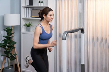 Enerjik ve güçlü atletik Asyalı kadın evde koşu makinası çalıştırıyor. Formda fiziğin takibi ve ev çalışması ve eğitimle sağlıklı yaşam tarzına bağlılık. Kuvvetli