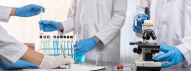 Kendini adamış bir grup bilim adamı yeni bir aşı ilacı ya da antibiyotik geliştirmek için tıbbi laboratuvarda mikroskop kullanarak kimyasal deney yapıyorlar. Biyoteknoloji laboratuvarı ve tıp araştırma konsepti. Neoterik