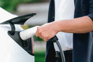 Yolculuk sırasında doğal orman ya da milli parktaki elektrikli araba için şarj olan bir adam. Tatil ve tatil boyunca çevre dostu seyahat. Yükselt