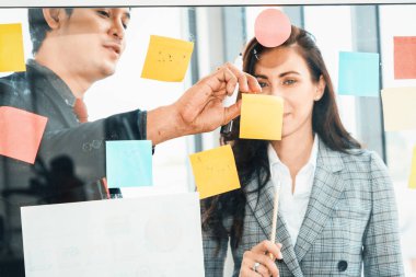 İş adamları ofisteki proje planlama kurulunda çalışıyor ve proje gelişimini analiz etmek için iş arkadaşlarıyla sohbet ediyorlar. Düzenli olması için cama yapıştırılmış yapışkan notlar kullanıyorlar. Jivy