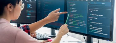 Kadın programcı bilgisayarda gösterilen kodu işaret ederken açıklıyor. Profesyonel programcı modern şirket ofisinde veri analizi ve Java betiği sunar. - Yakın çekim. Filizlenen.
