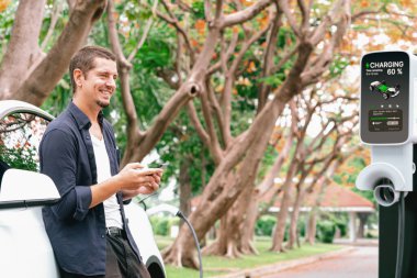 Adam sonbahar tatili tatilinde ulusal park ya da sonbahar ormanı gezisinde EV şarj istasyonundan elektrik aküsü almak için akıllı telefon internet bankacılık uygulaması kullanıyor. Yükselt