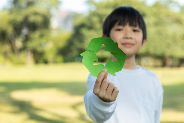 Cheerful young asian boy holding recycle symbol on daylight natural green park promoting waste recycle, reduce, and reuse encouragement for eco sustainable awareness for future generation. Gyre