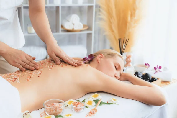 Closeup woman customer having exfoliation treatment in luxury spa salon with warmth candle light ambient. Salt scrub beauty treatment in health spa body scrub. Quiescent