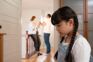 Stresli ve mutsuz genç kız köşeye kıvrılıp kulaklarını kapatarak arka planda ebeveyninin tartışmasını engelliyor. Evde aile içi şiddet ve travmatik çocukluk depresyona dönüşür. Eşzamanlama