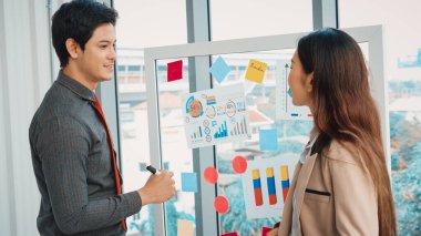 İş adamları ofisteki proje planlama kurulunda çalışıyor ve proje gelişimini analiz etmek için iş arkadaşlarıyla sohbet ediyorlar. Düzenli olması için cama yapıştırılmış yapışkan notlar kullanıyorlar. Jivy