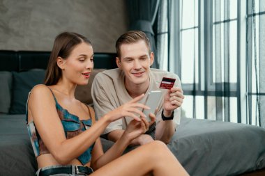 Genç çift, kredi kartıyla ödemek için internet üzerinden ödeme uygulaması ve dijital cüzdan kullanarak yatak odasında oturuyor. Mobil internet üzerinden alışveriş ve modern alımlar. Açılıyor
