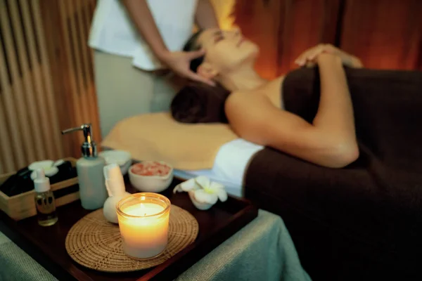 Aromatherapy massage ambiance or spa salon composition setup with focus decor candles and spa accessories on blurred woman enjoying blissful aroma spa massage in resort or hotel background. Quiescent