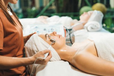 Güzeller güzeli beyaz kadın güzellik teçhizatı ve tıbbi ekipmanlarla çevrili modern kaplıca salonundaki profesyonel eller tarafından masaj yaptırırken spa yatağında uzanıyor. Kapatın. Huzur