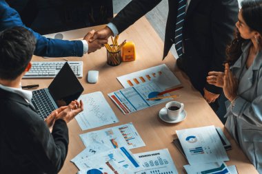 Grup iş adamları toplantı masasında el sıkışırken üst açıdan kendilerine güvenirler. Genç işadamı ve işkadını işçiler yatırım anlaşması imzaladılar. Jivy