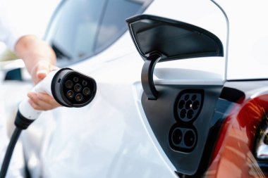 Dışarıdaki şarj istasyonundan EV şarj aletini şarj etmek için elektrikli araca elle tak. Alternatif temiz ve sürdürülebilir enerji kavramına sahip taze gün ışığı ortamı. Kalıcı