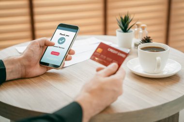 Masada oturan genç adam kredi kartıyla ödeme yapmak için akıllı telefondaki dijital cüzdanı ve uygulamayı kullanıyor. Mobil internet üzerinden alışveriş ve modern alımlar. Açılıyor