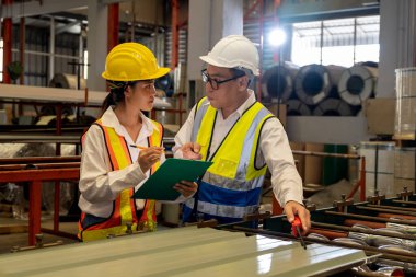 Fabrika mühendisi, metal levha ürünü üzerinde kalite kontrolü yapmak ve ağır endüstriyel çelik damgalama veya oluşturma makinesini denetlemek için iş arkadaşıyla işbirliği yapar. Örnek gösteriliyor
