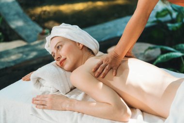 Güzel genç bir kadın, profesyonel masözden kaplıca yatağına sırt masajı almış. Çekici bir kadın masaj terapistinin yetenekli elleriyle derin bir şekilde rahatlar. Doğayla çevrili. Huzur.