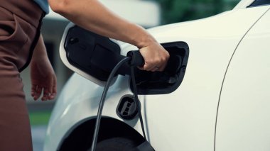 İlerici kadın evdeki elektrikli aracına şarj istasyonu fişi takıyor. EV otomobilleri çevreye yararlı temiz ve yeşil enerji kavramı sağlar.