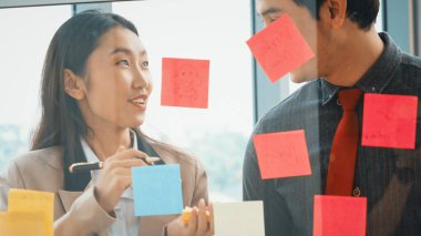 İş adamları ofisteki proje planlama kurulunda çalışıyor ve proje gelişimini analiz etmek için iş arkadaşlarıyla sohbet ediyorlar. Düzenli olması için cama yapıştırılmış yapışkan notlar kullanıyorlar. Jivy