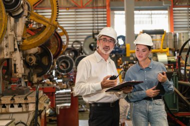 Metal imalatında makine mühendisliği denetleyicisi olarak liderlik örneğini sunan çelik endüstriyel makineyi incelemek için dizüstü bilgisayar kullanan fabrika mühendisi ve asistan..