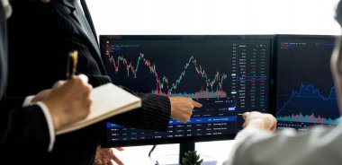 Bir grup meslek tüccarı borsa yatırımları hakkında tartışırken, bilgisayarda gösterilen artan finans grafiğini işaret ediyorlar. Hisse senedi yatırım konsepti eksildi. Filizlenen.