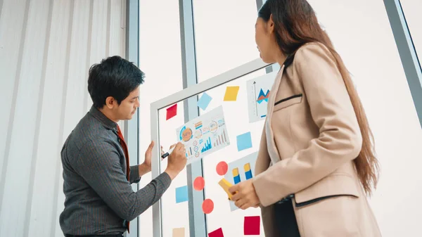 Business people work on project planning board in office and having conversation with coworker friend to analyze project development . They use sticky notes posted on glass to make it organized. Jivy