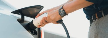 Genç adam, şehrin ticari otoparkındaki şarj istasyonundan elektrikli araba aküsünü şarj etmek için EV şarj aleti koymuş. Sürdürülebilir çevre dostu şehir yolculuğu için şarj edilebilir EV araba. Yararlı
