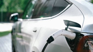 Yazın yeşil sürdürülebilir şehir bahçesinde elektrikli araba şarj oluyor. Kentsel sürdürülebilirlik yaşam tarzı yeşil temiz yeniden şarj edilebilir enerji elektrikli BEV araç iç organları