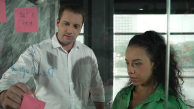 Yetenekli işadamı, cam duvara renkli yapışkan notlar yapıştırarak proje yöneticisine pazarlama fikrini sundu. Proje yöneticisi yatırımcıya projeyi gösteriyor, anlatıyor, gösteriyor. Yönlendirici.