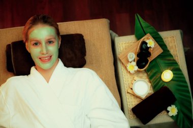 Kaplıca salonunun sakin atmosferi, kadın müşterinin gülümsemesi ve sıcak mum ışığında lüks yüz kremi masajıyla gençleşmesi. Yüz bakımı ve güzellik konsepti. Sessiz.