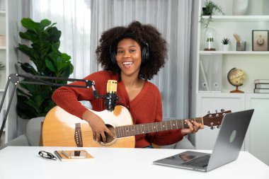 Genç Afrikalı Amerikalı müzisyenin sunucu kanalı gitar çalıyor, şarkı söylüyor, stüdyoda dizüstü bilgisayardan yayın yapıyor. Kulaklık dekorasyonu ve mikrofon kaydı. Tatlandırıcı.