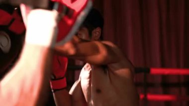 Asyalı ve Kafkasyalı Muay Thai boksörü boks antrenmanında boks antrenmanında boks antrenörüne yumruk atma, Muay Thai boks tekniği ve becerilerini sergileme. Impetus