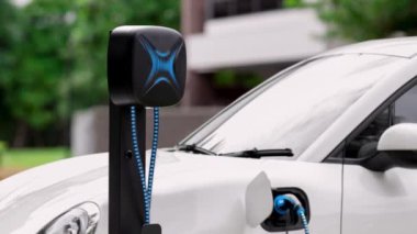 Elektrikli araba EV şarj kablosu ile şarj olmak için şarj istasyonuna bağlı. Geleceğin yenilikçi EV arabası ve enerji sürdürülebilirliği. Akıllı ve fütüristik ev enerjisi altyapısı. İnceleyin