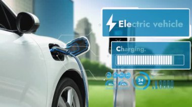 EV otomobili, elektrik yükleme istasyonuna bağlanarak yeşil parktaki EV şarj cihazının pil durumu hologramını şehrin gelecekteki ekolojik yaşam biçimi ve temiz enerjinin kullanımı olarak gösteriyor. İnceleyin
