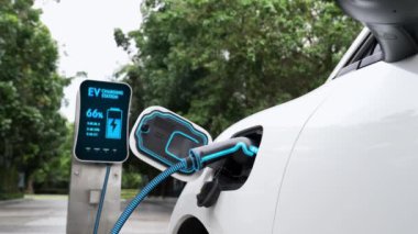 Doğal yeşil araba parkındaki ekolojik temiz enerji şarj istasyonundan gelen fütürist akıllı EV şarj aletinin şarj ettiği elektrikli araba. Alternatif enerji kullanan gelecekçi çevre dostu elektrikli araba. İnceleyin