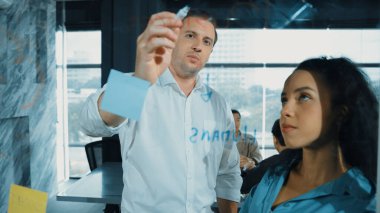 Yetenekli işadamı, cam duvara renkli yapışkan notlar yapıştırarak proje yöneticisine pazarlama fikrini sundu. Proje yöneticisi yatırımcıya projeyi gösteriyor, anlatıyor, gösteriyor. Yönlendirici.