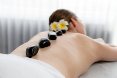 Lüks tatil köyündeki kaplıcalarda sıcak taş masajı. Gün ışığı sükunet ortamında, mutlu kadın müşteri bazalt taş masajından zevk alıyor. Rahatlatıcı bir sıcaklıkla vücudun üzerinde süzülüyor. Sessiz.