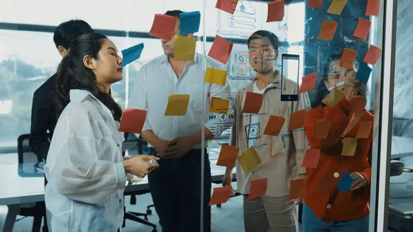 Portrait of professional business team brainstorming marketing idea by using sticky notes to share creative idea at glass wall. Group of diverse business team discuss about strategy. Manipulator.