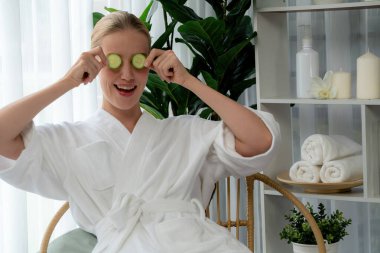 Elinde taze salatalık dilimleri tutan ve bornoz giyen bir kadın tatil köyünde ya da otelde lüks yüz derisi kaplıcalarının tadını çıkarıyor. Yüz ve güzellik tedavisi için cilt bakımı. Sessiz.