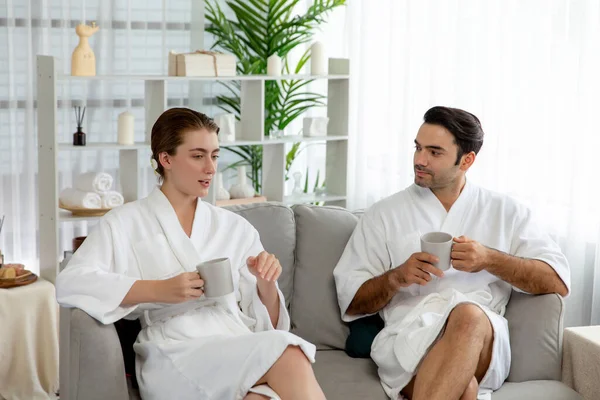 Beauty or body treatment spa salon vacation lifestyle concept with couple wearing bathrobe relaxing with drinks in luxurious hotel spa or resort room. Vacation and leisure relaxation. Quiescent