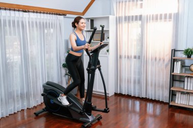 Enerjik ve güçlü atletik Asyalı kadın evde eliptik koşu makinesiyle koşuyor. Formda fiziğin takibi ve ev çalışması ve eğitimle sağlıklı yaşam tarzına bağlılık. Kuvvetli