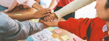 A group of business people putting their hands together at meeting room on table with mind map scatter around. Startup group showing unity teamwork and friendship. Close up. Focus on hand. Variegated. clipart