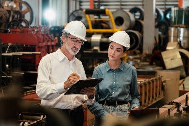 Metal imalatında makine mühendisliği denetleyicisi olarak liderlik örneğini sunan çelik endüstriyel makineyi incelemek için dizüstü bilgisayar kullanan fabrika mühendisi ve asistan..