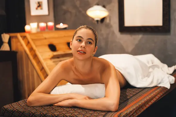 Portrait of beautiful caucasian woman in white towel woman lies on spa bed in front of warm wooden sauna cabinet with relaxation and peaceful at spa salon. Close up. A Side view. Tranquility.