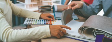 Yetenekli iç dizayn ekibi perde malzemelerini dikkatle seçerken iş arkadaşı da toplantı masasının üzerinde ev modeliyle perdenin rengini seçiyor. Yaratıcı tasarım konsepti. Değiştirilmiş.