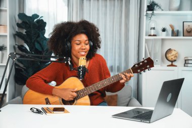 Genç Afrikalı Amerikalı müzisyenin sunucu kanalı gitar çalıyor, şarkı söylüyor, stüdyoda dizüstü bilgisayardan yayın yapıyor. Kulaklık dekorasyonu ve mikrofon kaydı. Tatlandırıcı.