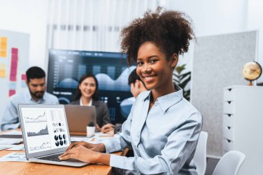 Bir grup ofis çalışanı ile birlikte arka planda ekranda gösterim paneliyle buluşan mutlu Afrikalı genç bir iş kadını portresi. Takım toplantısında kendine güveni tam bir ofis hanımı. Uyum