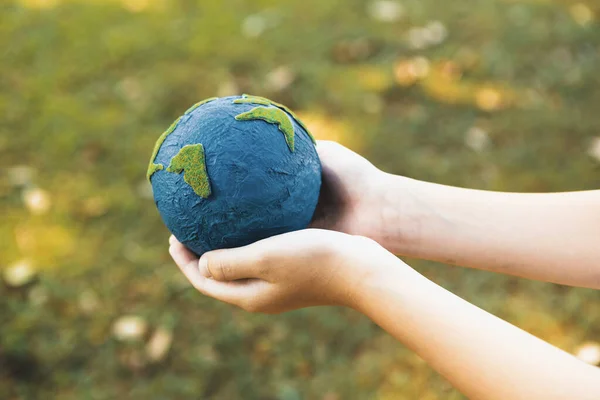 Young boys hand holding planet Earth globe at natural park background as Earth day to save this planet with ESG principle and environment friendly energy for brighter future. Gyre