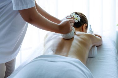 Sıcak bitkisel top spa masaj vücut tedavisi, masör kadın vücuduna nazikçe şifalı bitki torbası bastırıyor. Aromaterapi dinlenme sükuneti ve sükuneti kaplıca salonundaki atmosferi aydınlatıyor. Sessiz.