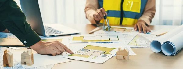 Skilled engineer uses divider to measure the blueprint while architect pointing the mistake point in the building blueprint on table with architectural document scatter around. Close up. Delineation.