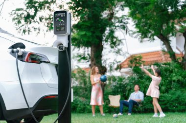 Evde şarj edilen elektrikli araba şarjını mutlu ve neşeli bir ailenin arka planına odakla. EV arabası daha iyi bir gelecek için alternatif ve sürdürülebilir enerji kullanıyor.
